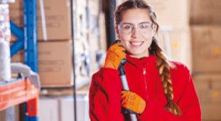 Une femme souriante, vêtue d'un manteau rouge, dans un entrepôt.