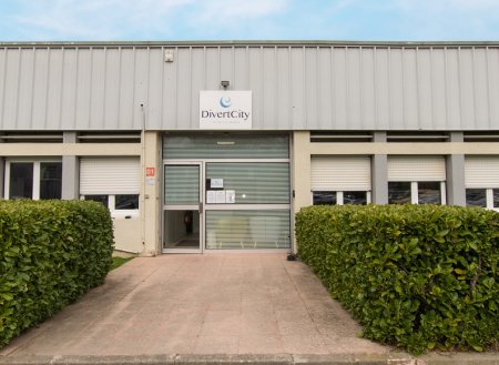 Bâtiment industriel avec entrée double porte vitrée et bushes vertes à l'avant.